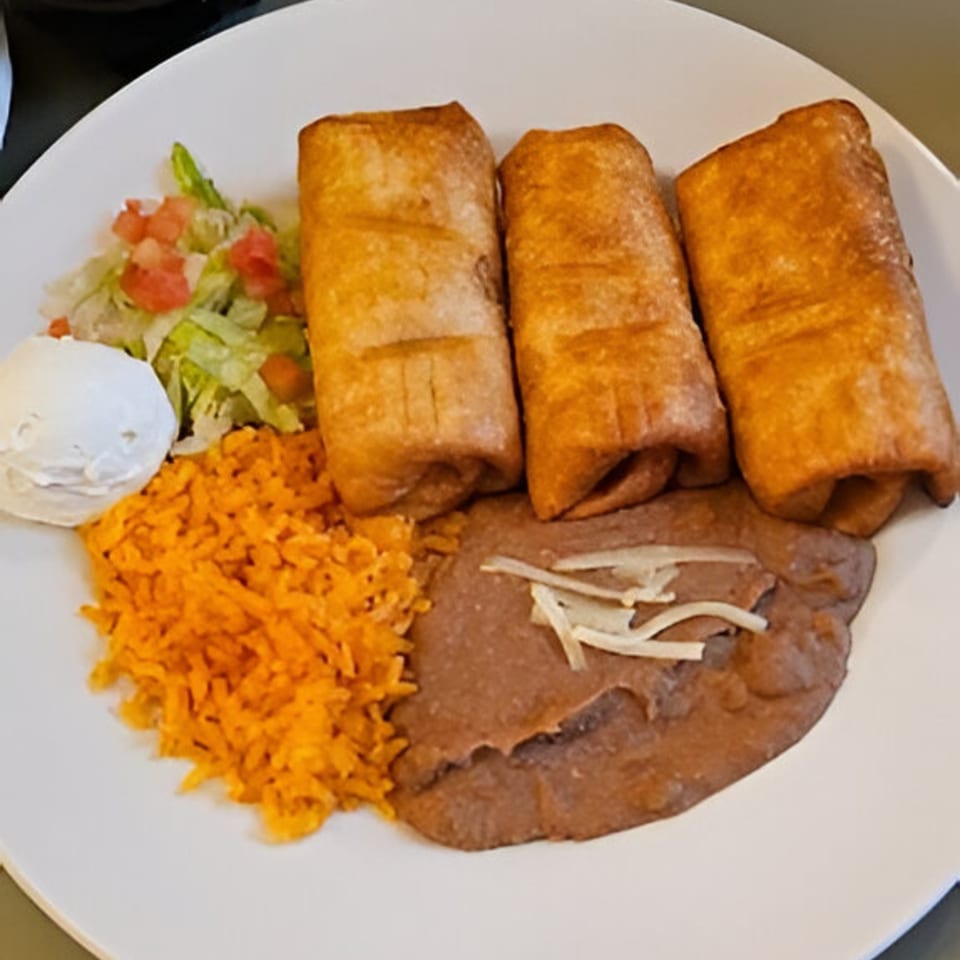 Three golden-brown chimichangas with rice, refried beans, shredded lettuce, diced tomatoes, and sour cream.