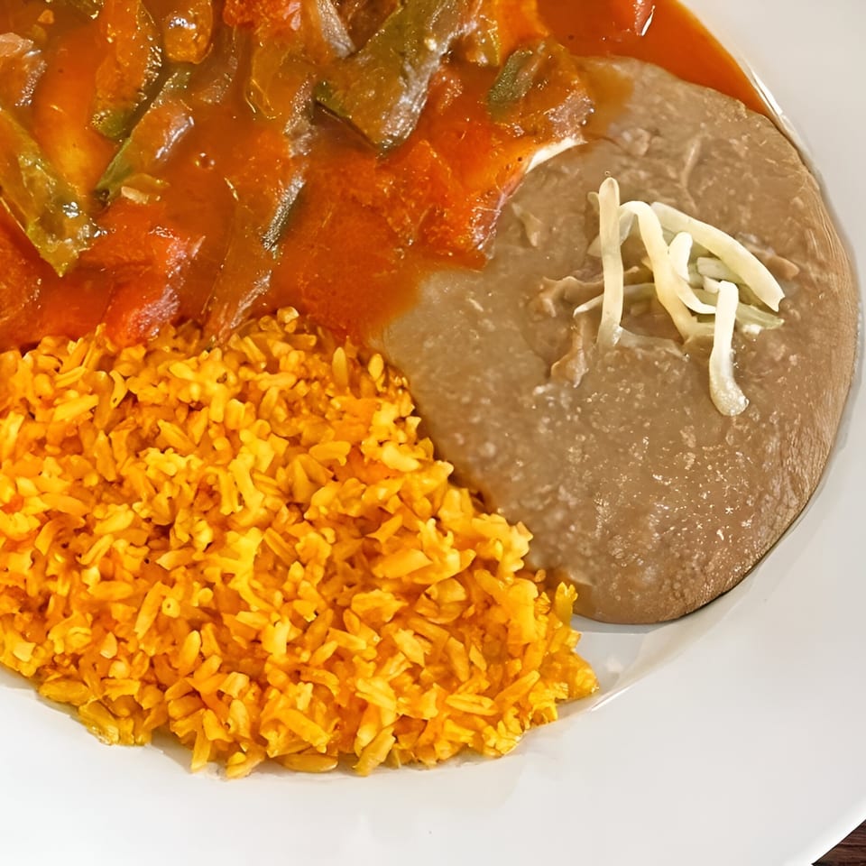 Dos Banderas' Mexican dish with orange rice, refried beans topped with cheese, and a red stew.